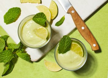 avocado lime smoothie on a white cutting board with limes and a knife on a green table
