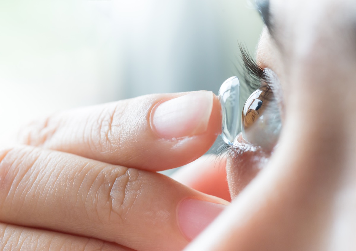 woman putting contact lens in her right eye,