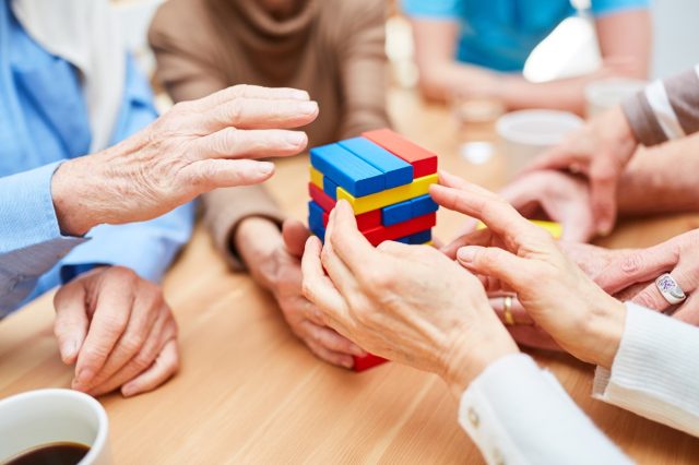 Een groep ouderen met dementie bouwt een toren in een verpleeghuis van gekleurde bouwstenen