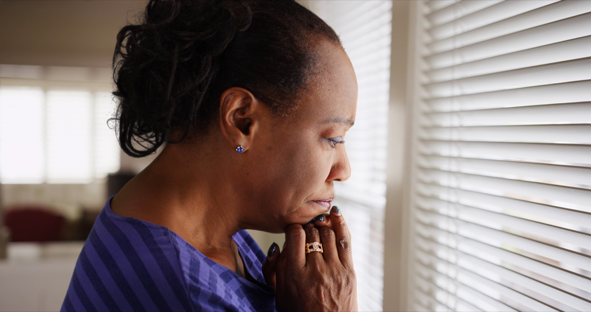 An older black woman mournfully looks out her window - Image