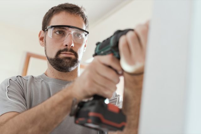 repairman with protective goggles, he is using a drill and doing a home renovation