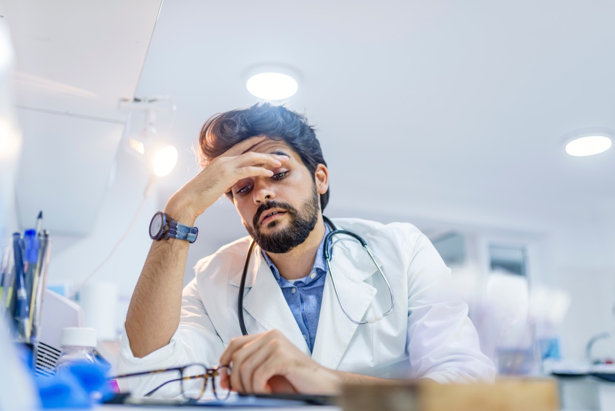 Stressed male doctor sat at his desk. Mid adult male doctor working long hours. Overworked doctor in his office. Not even doctors are exempt from burnout