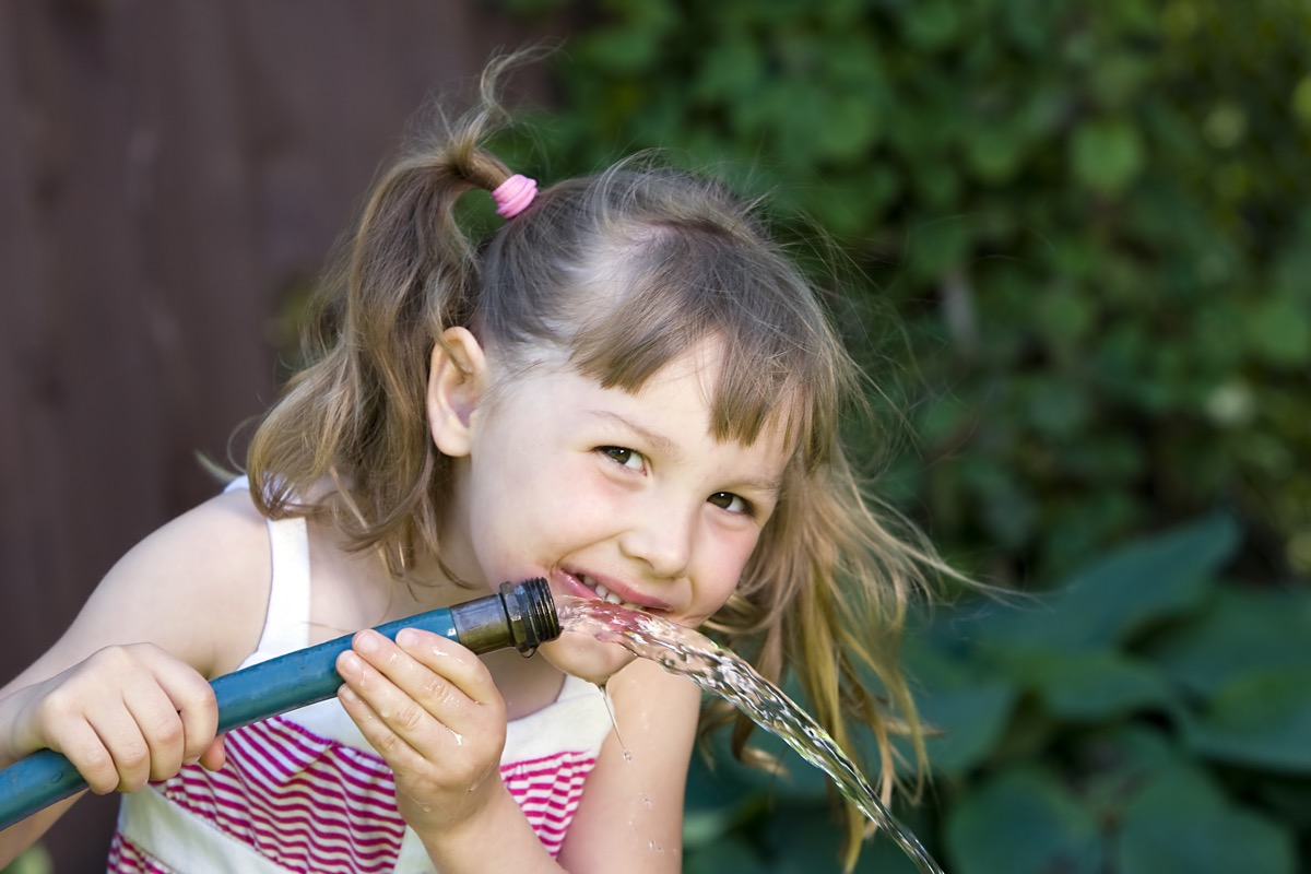 child drinking from a garden hose