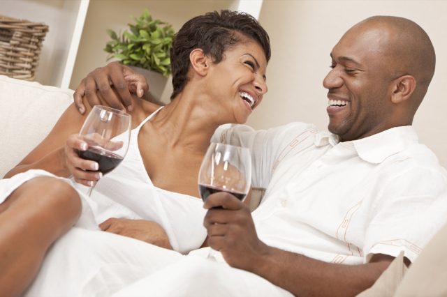 the couple laugh together at home and drink red wine
