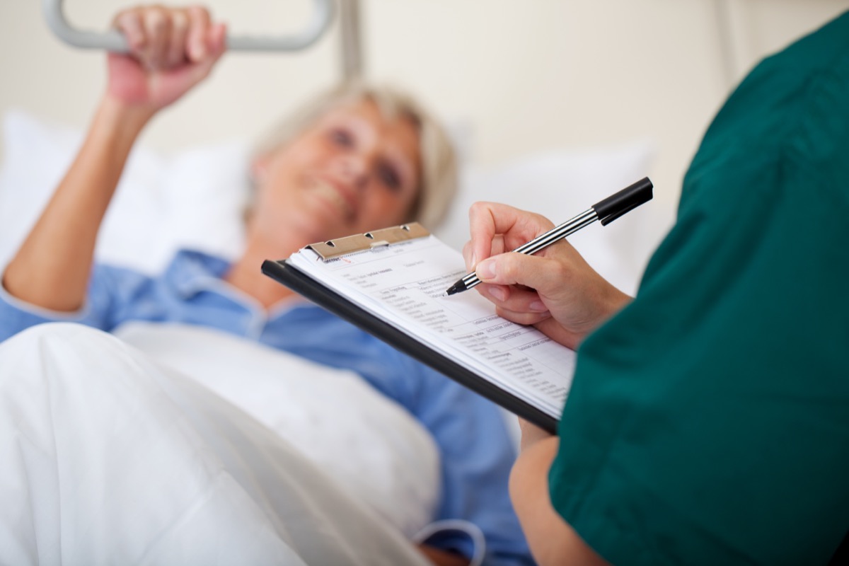 Mid adult female nurse writing on clipboard while looking at patient in hospital