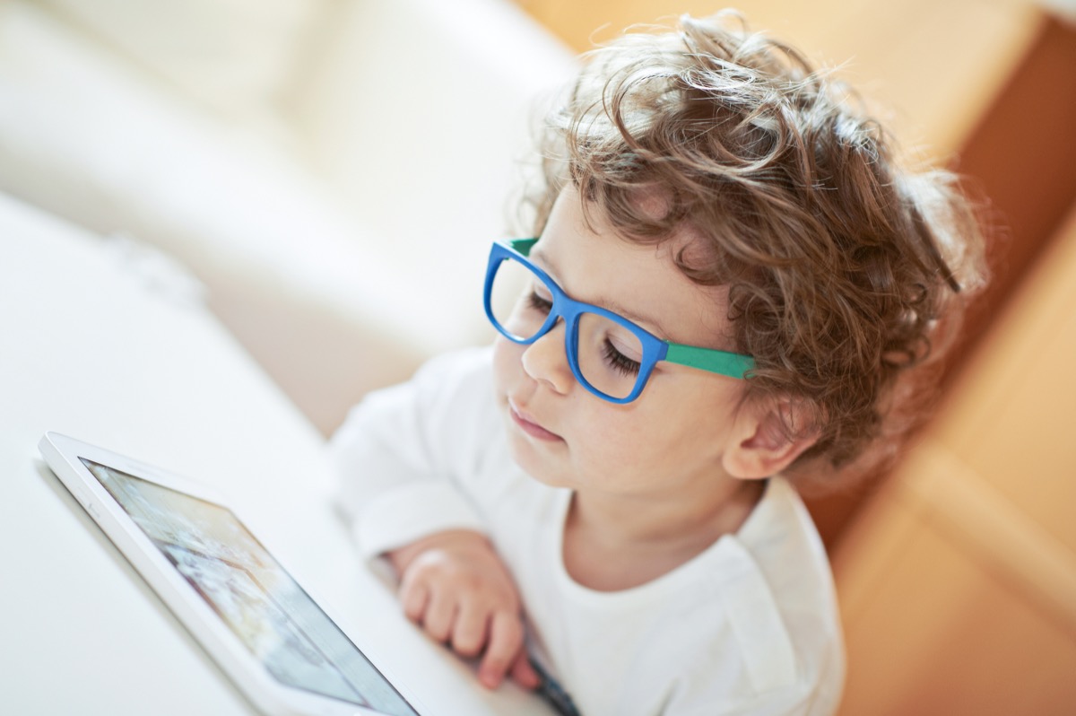 Boy in white t-shirt, wearing glasses, watching movie on tablet