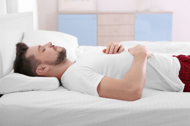 Young man lying on bed with orthopedic pillow at home