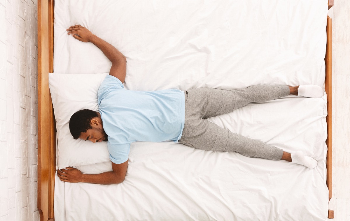 African american millennial guy sleeping, lying on stomach in bed