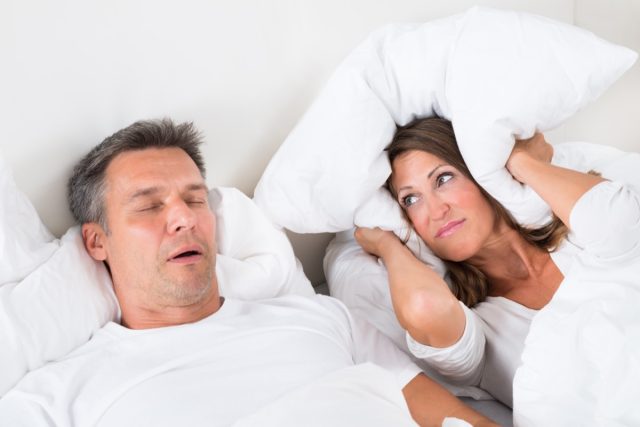 Woman Covering Her Ears With Pillow While Man Snoring