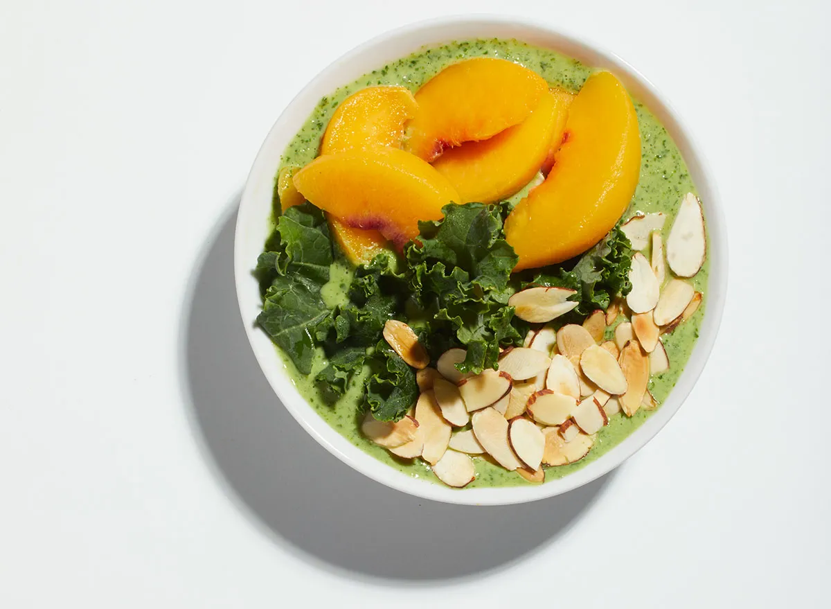 peaches and green kale smoothie bowl on white background