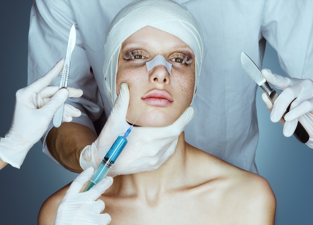 Patient in bandages. Nurses holding scalpel and syringe near her face
