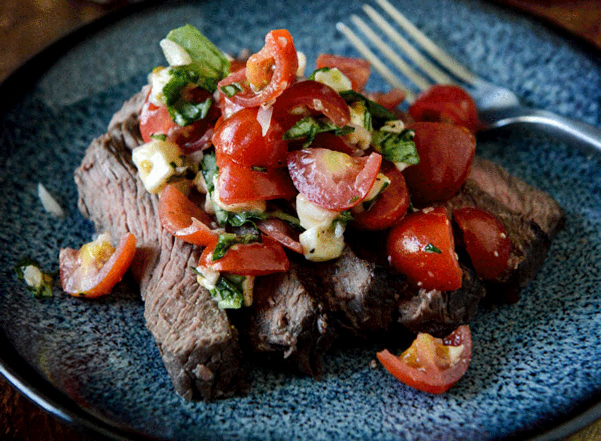 red wine marinated flank stake with cherry tomato caprese salsa on a dark plate and background