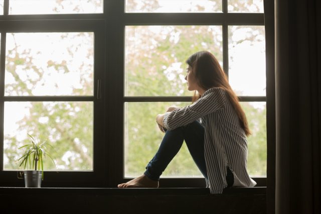 Pensive girl sitting on doorstep hugging knees looking at window, sad depressed teenage girl spending time alone at home, young upset pensive woman feeling lonely or frustrated thinking about problems