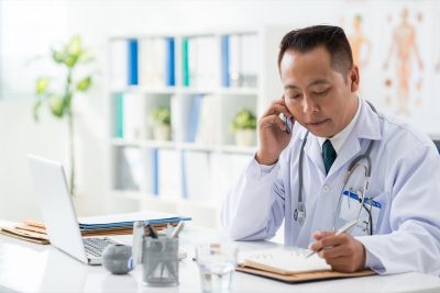 Doctor checking his daily planner when talking to his patient on the phone