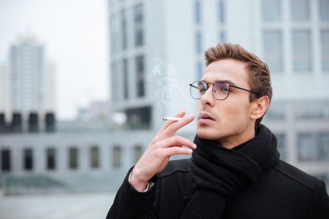 Business man in glasses and warm clothes smoking cigarette on the street