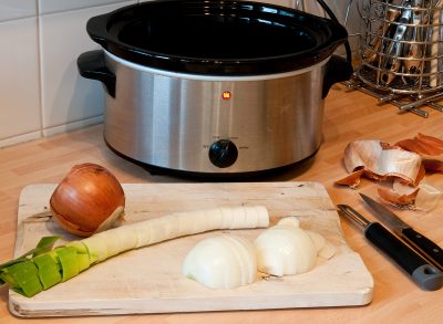 empty slow cooker with leeks and onions on cutting board