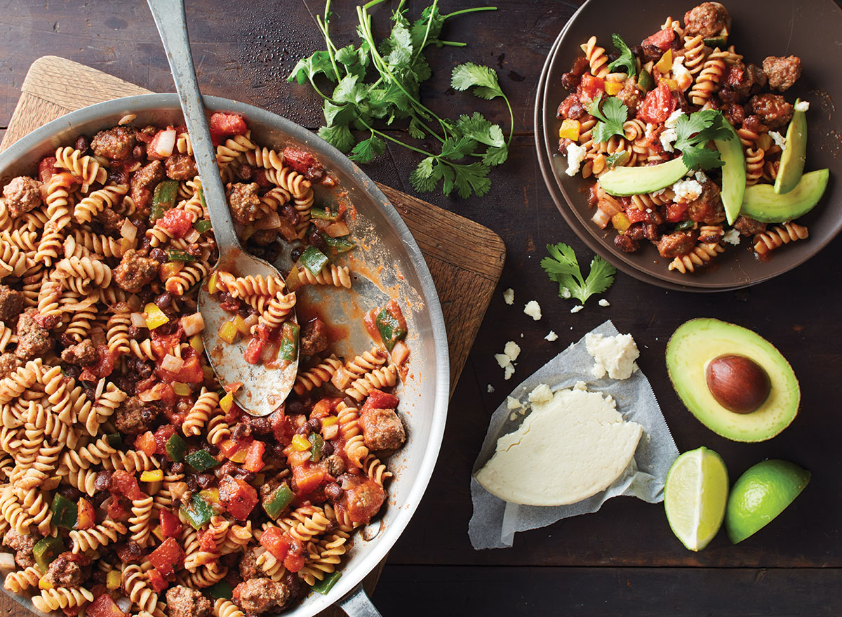 one skillet taco pasta with spoon, cotija cheese, and sliced avocado