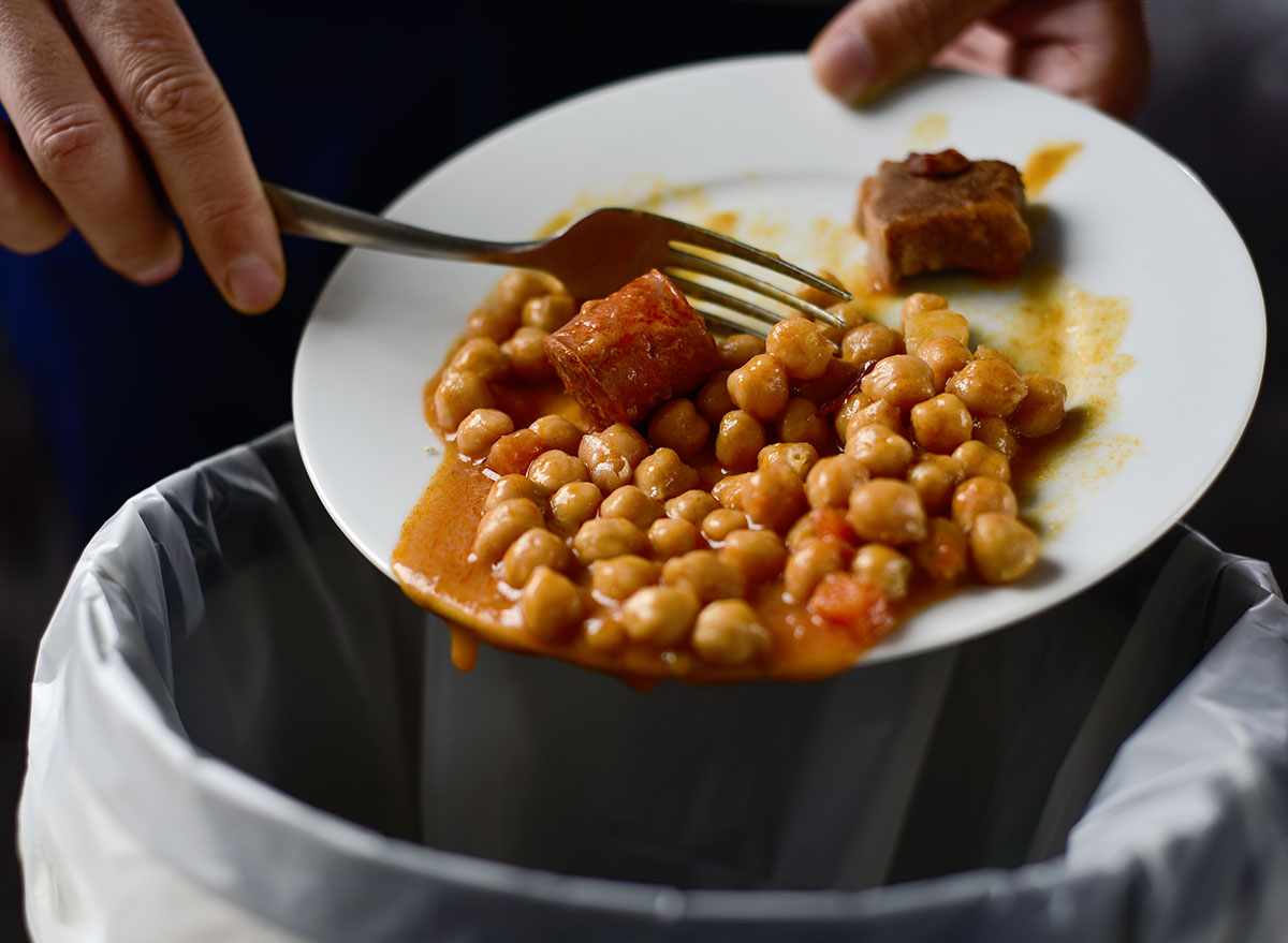 hands dumping leftovers in trash can from plate