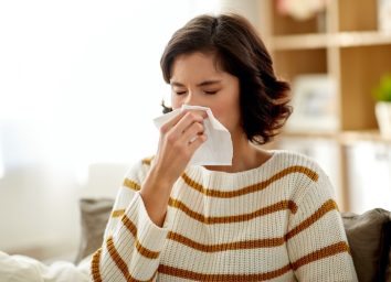 Sick woman blowing her runny nose in paper tissue at home.