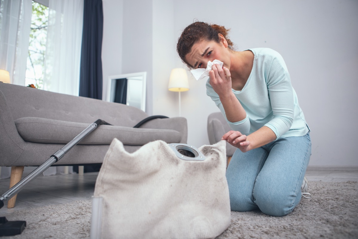 woman being prone to dust allergies suffering from consequences of not wearing any personal protective equipment while cleaning dirty carpet