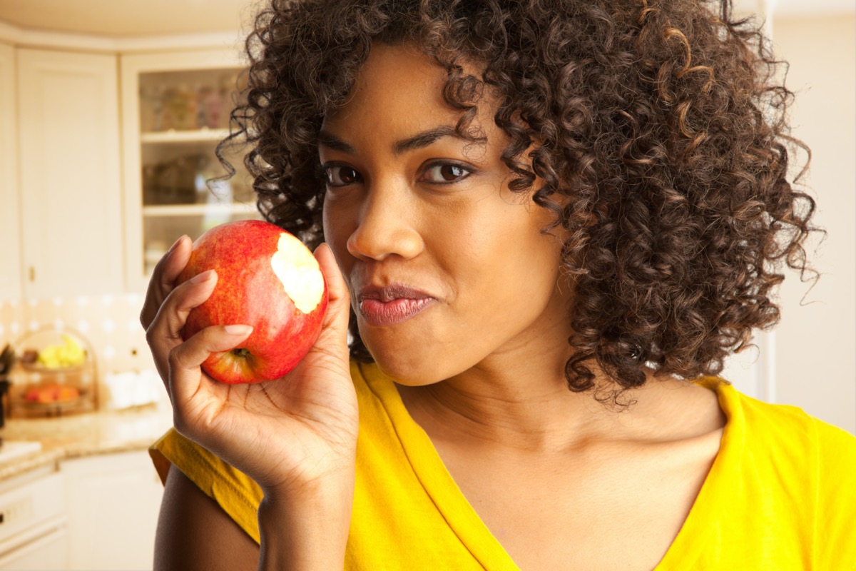 woman eating fresh red apple inside house kitchen