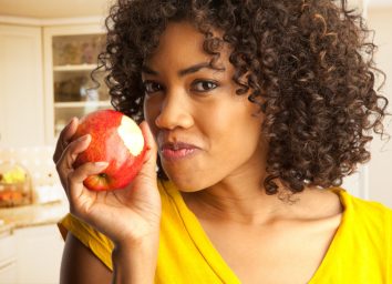 woman eating fresh red apple inside house kitchen