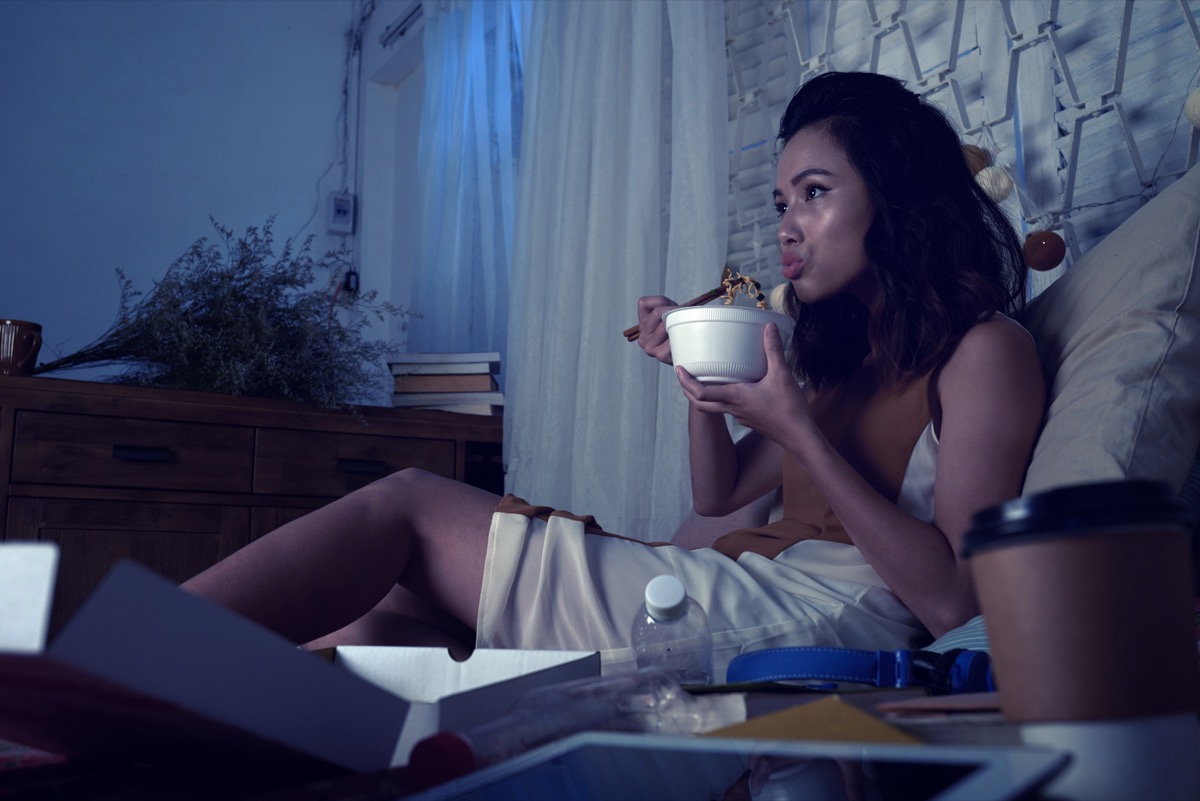 woman eating ramen soup and watching tv series late at night