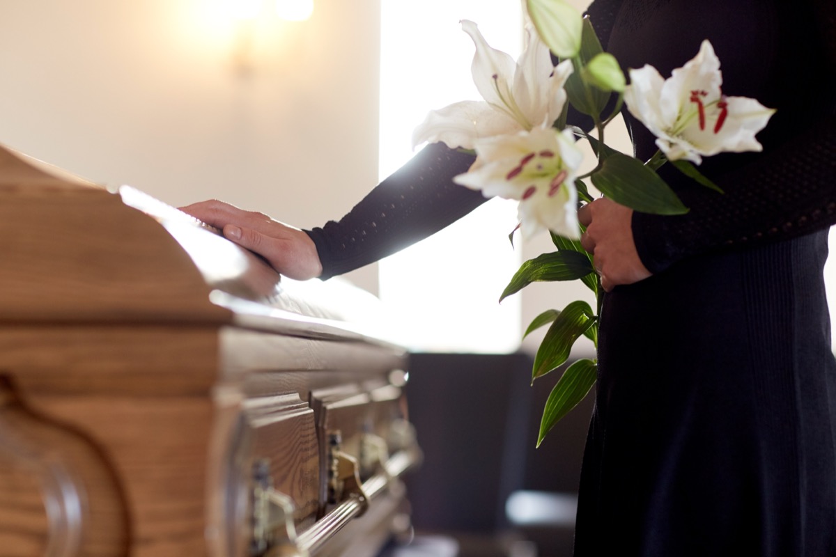 woman with white lily flowers and coffin at funeral in church