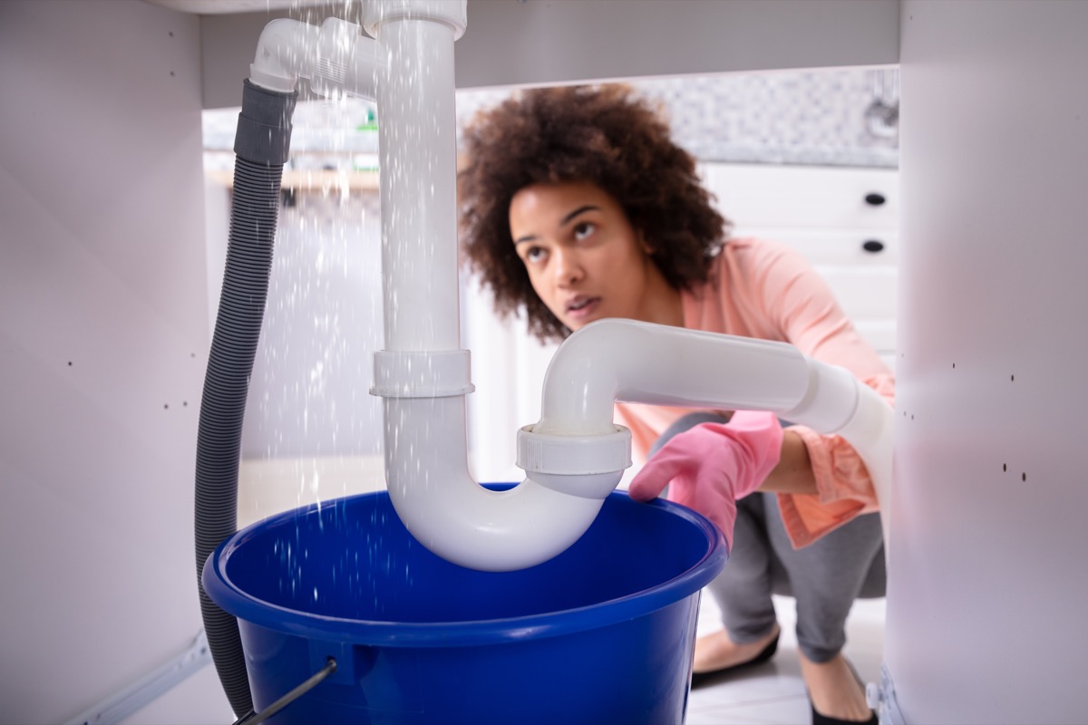 Woman Looking At Water Leaking From Sink Pipe