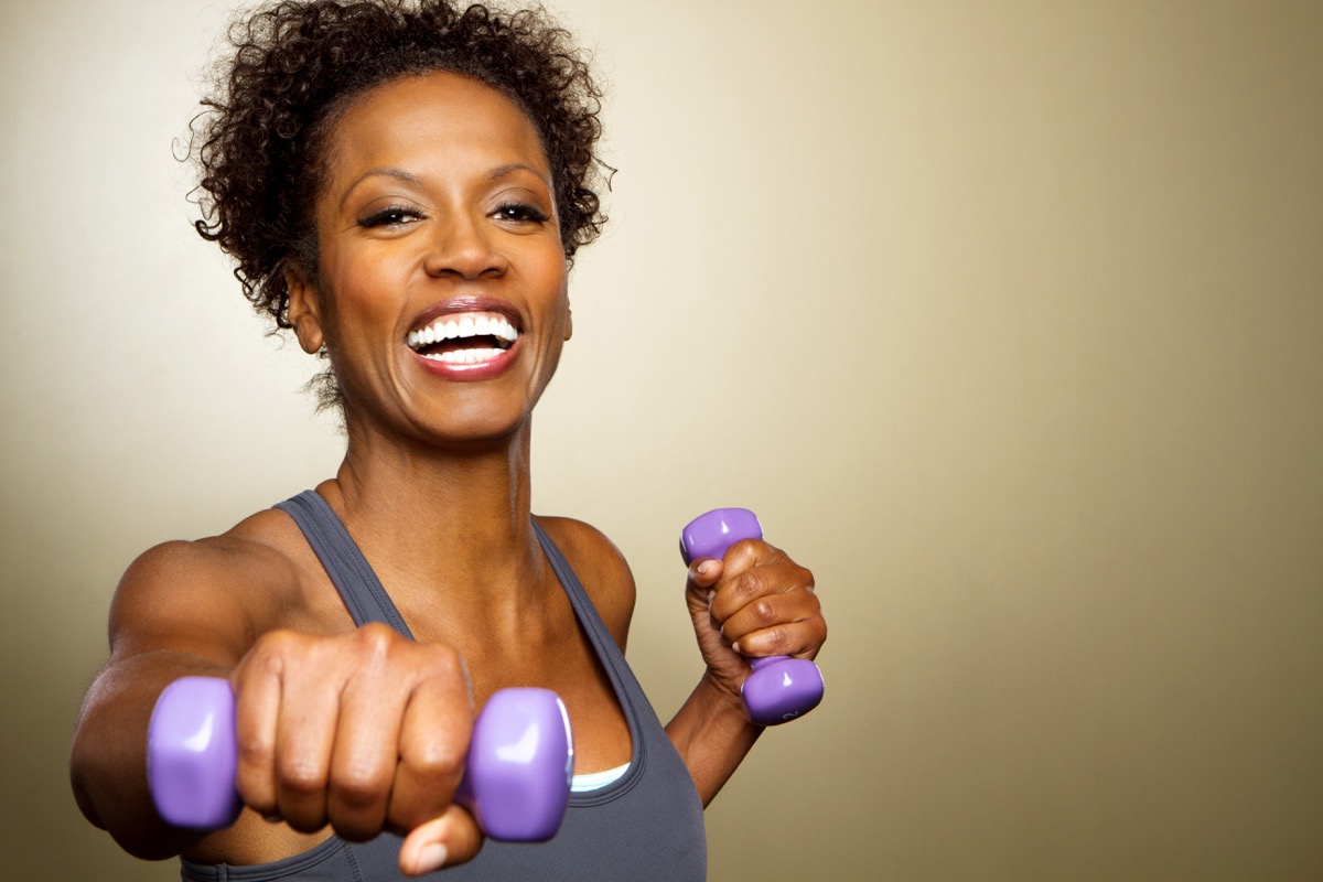 Happy African American fitness woman lifting dumbbells smiling and energetic