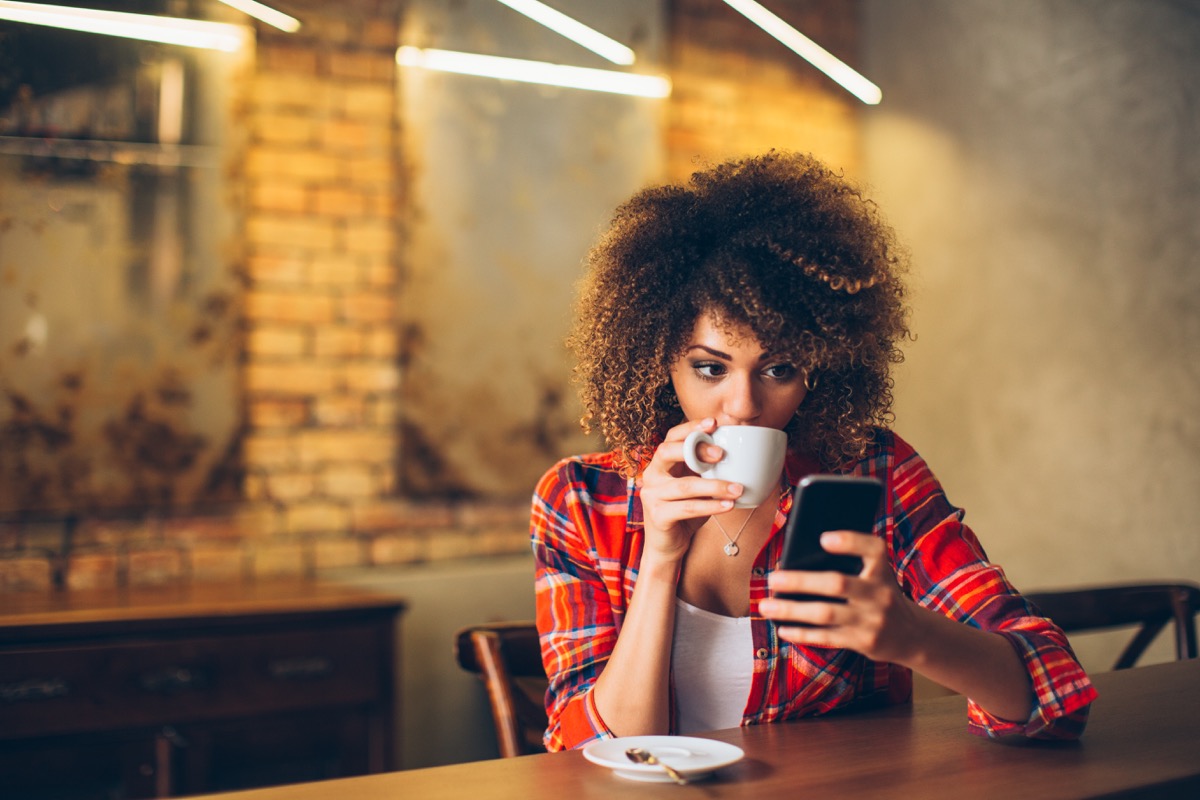 woman at cafe drinking coffee and using mobile phone