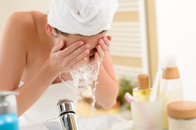 Frau spritzt Wasser über Waschbecken ins Gesicht