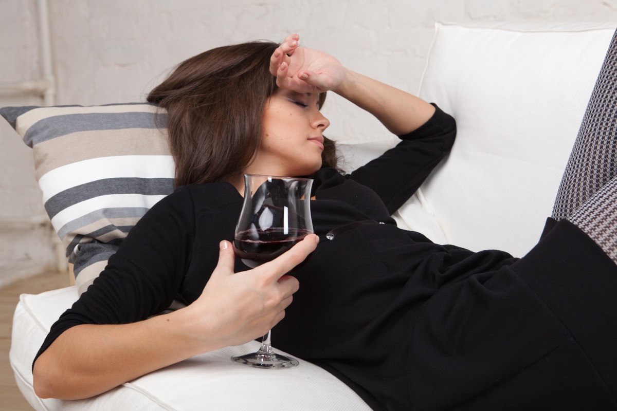 Young woman relaxes at home on the white sofa with a glass of red wine