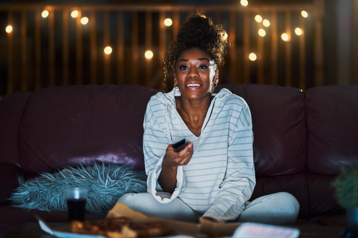 woman in pajamas staying up late at night eating pizza and watching tv