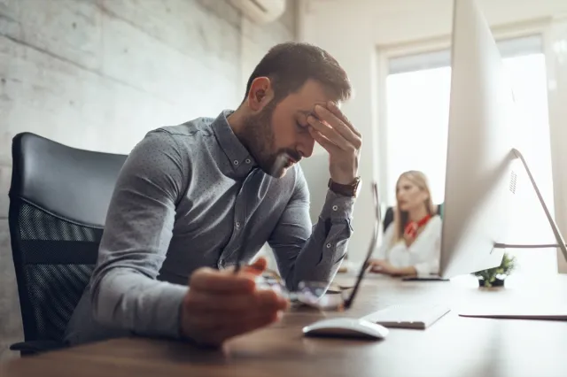 frustrated and stressed businessman sitting at the office front holding a computer and holding his head