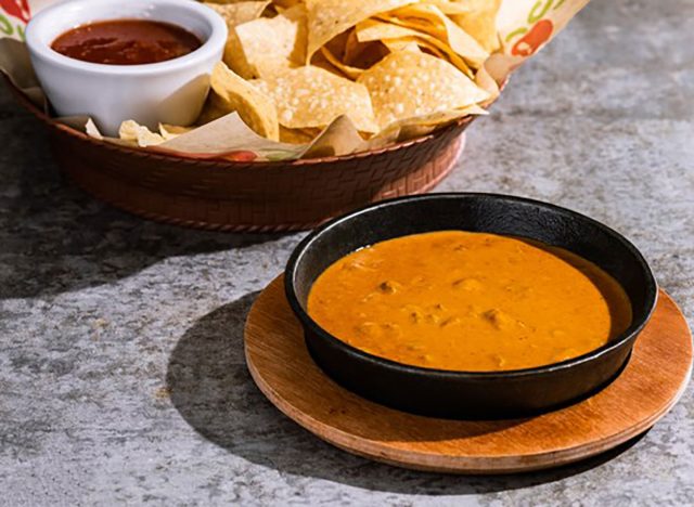 bowl of chilis skillet queso with basket of tortilla chips and salsa