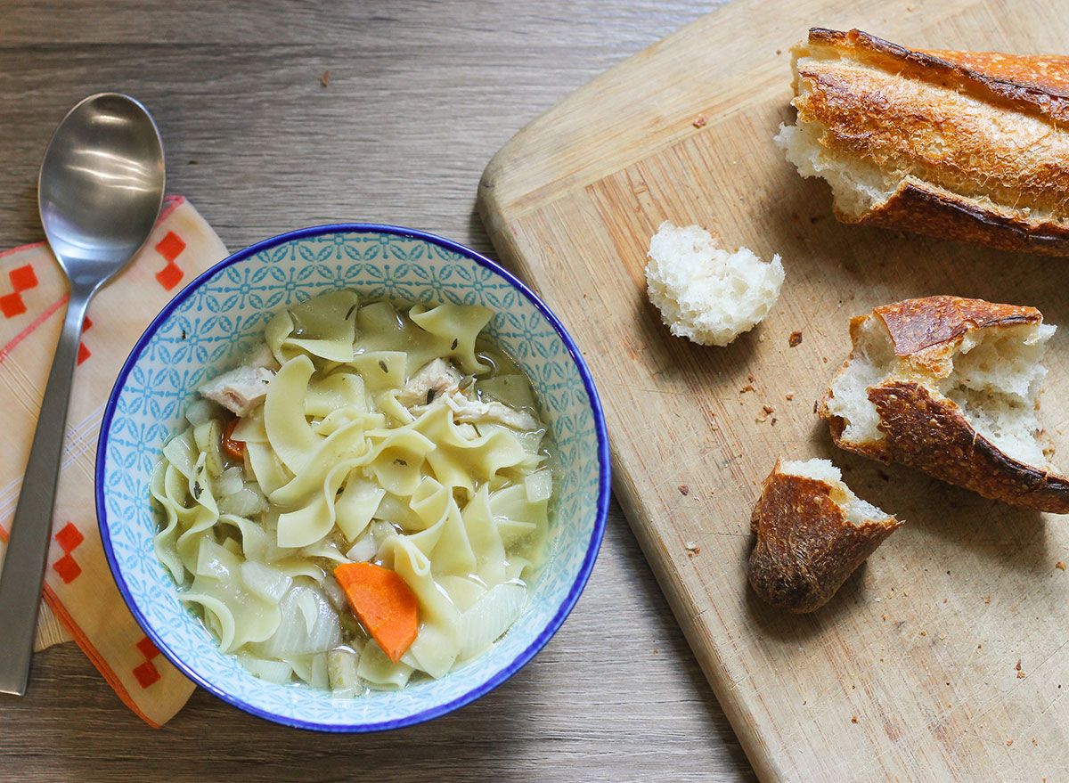Slow cooker chicken noodle soup with bread on a table.