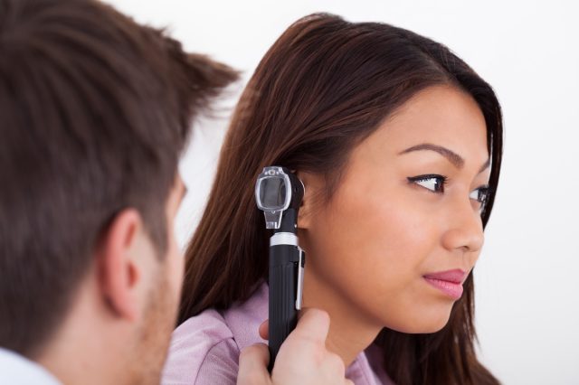 male doctor examining patient's ear with otoscope in clinic