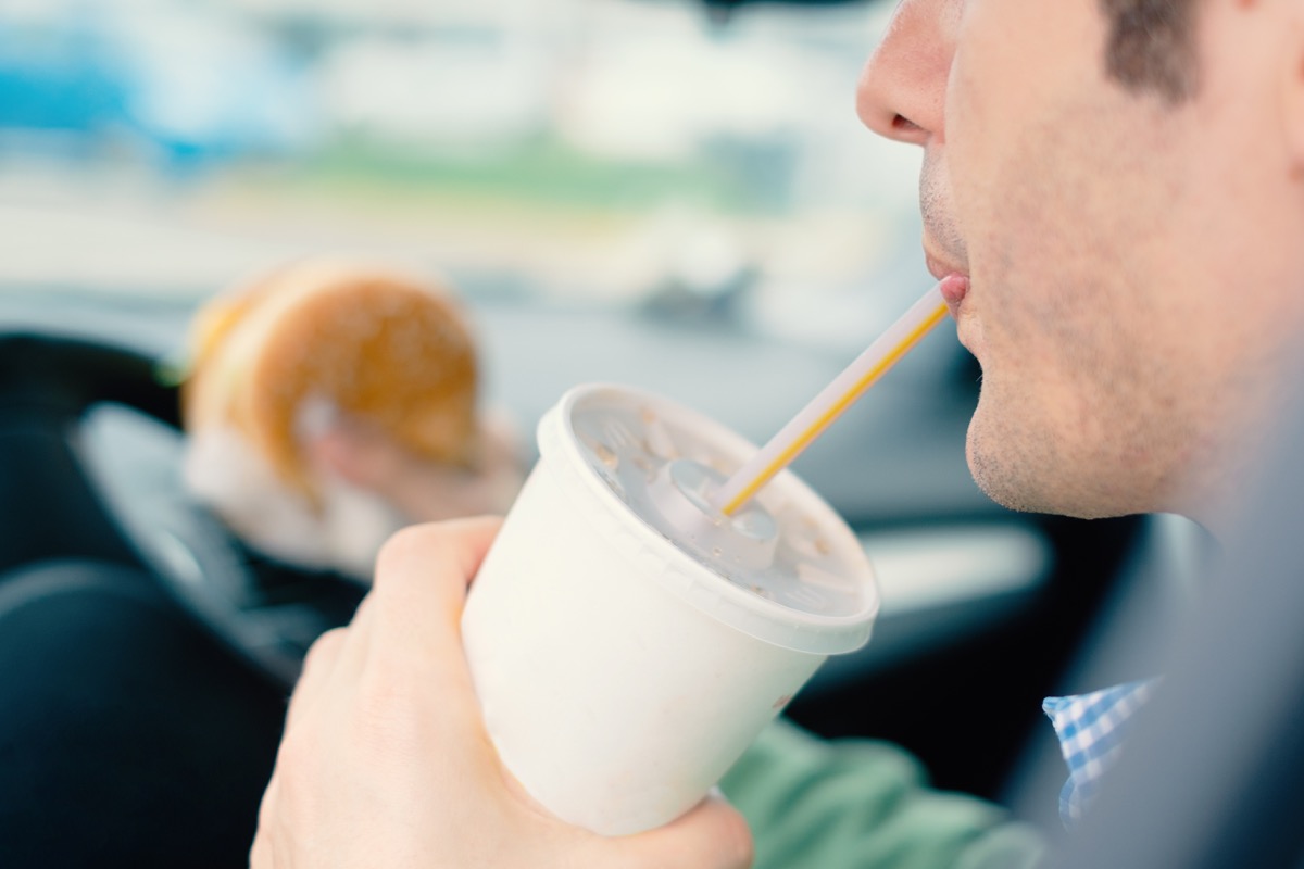 Man is dangerously eating junk food and cold drink while driving his car