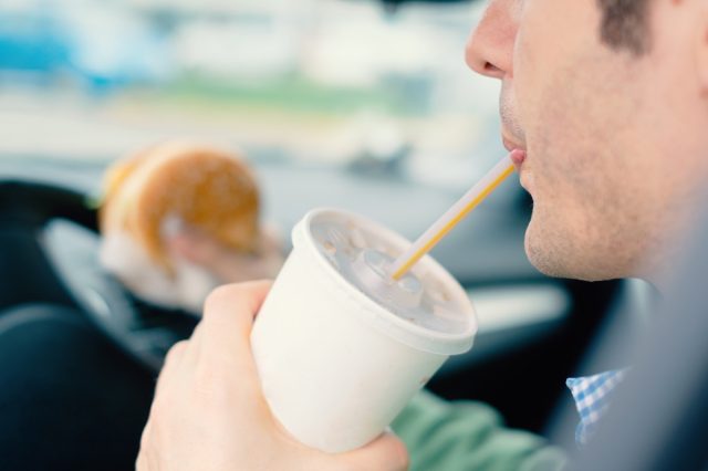 Mand, der farligt spiser junkfood og kolde drikke, mens han kører bil