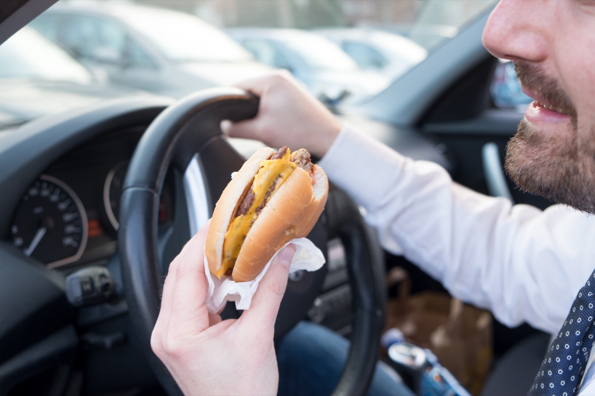 Man eats hamburger while driving a car