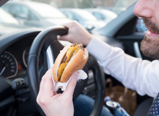 Man eating an hamburger while driving car