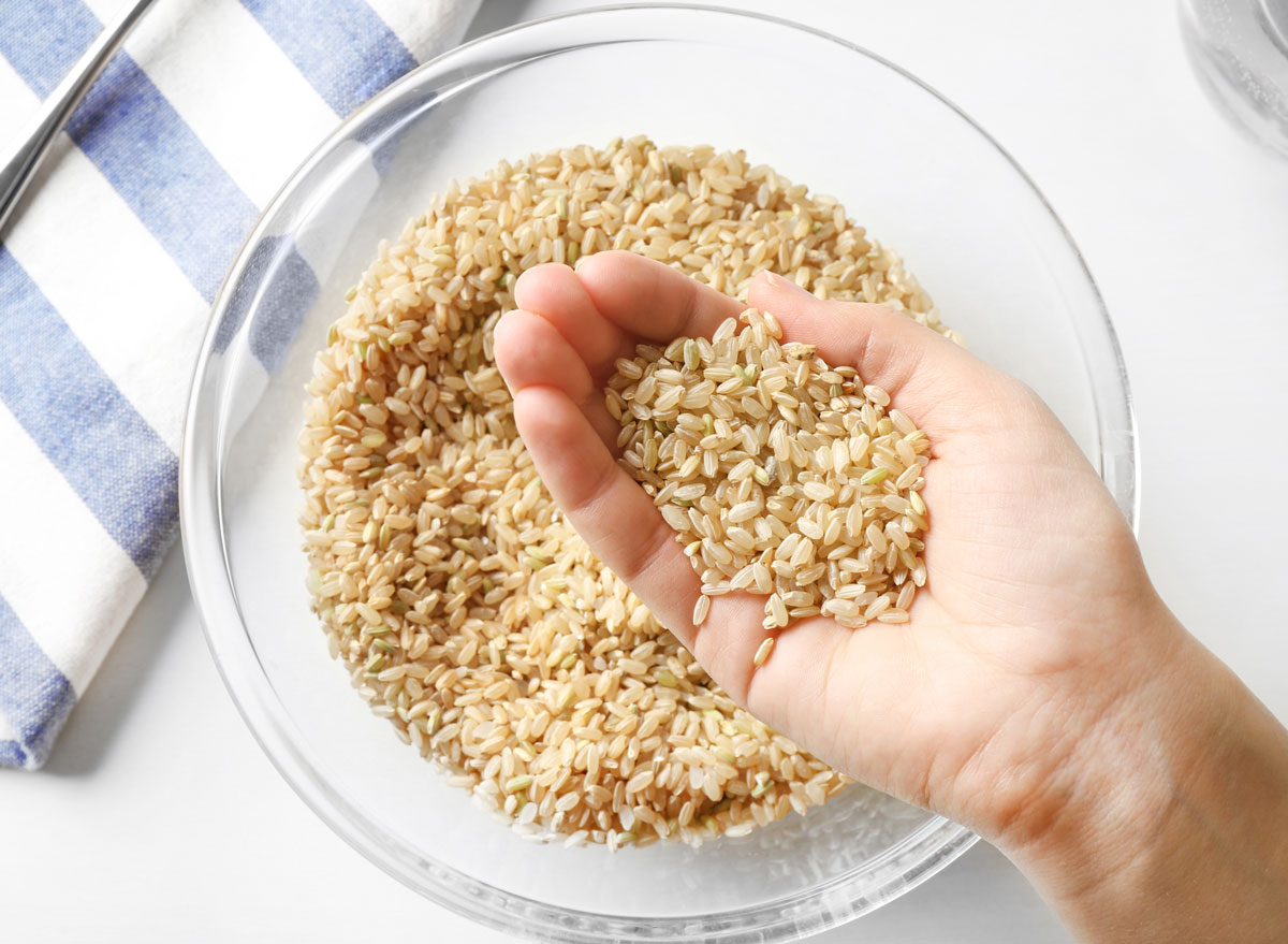 Holding brown rice in hand over a glass bowl of rice