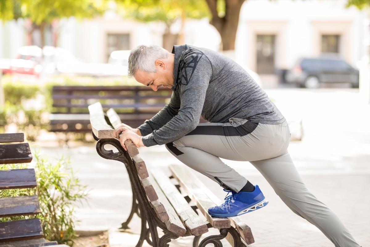 middle aged man stretching on park bench