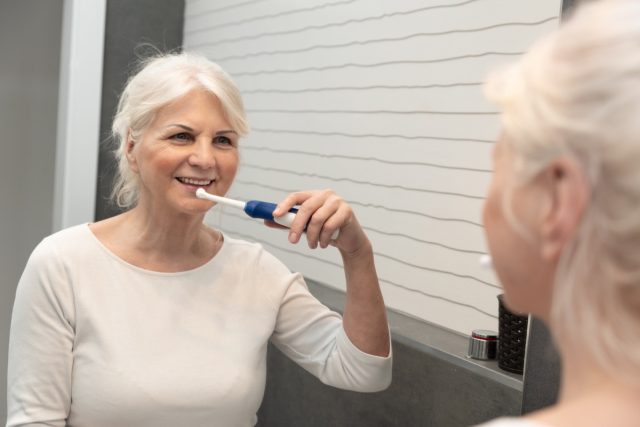 mature woman brushing teeth. Electric toothbrush used by senior woman