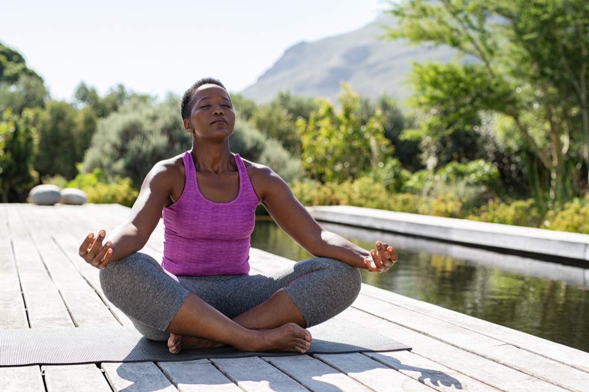 Mature african woman practicing yoga and meditates near swimming pool outdoor