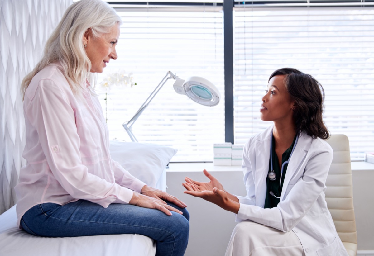 Mature Woman In Consultation With Female Doctor Sitting On Examination Couch In Office
