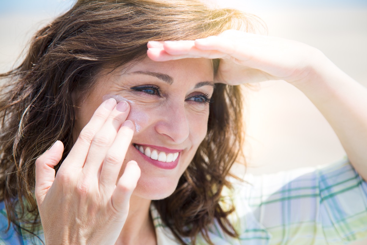 middle aged woman applying sunscreen lotion on face on the beach