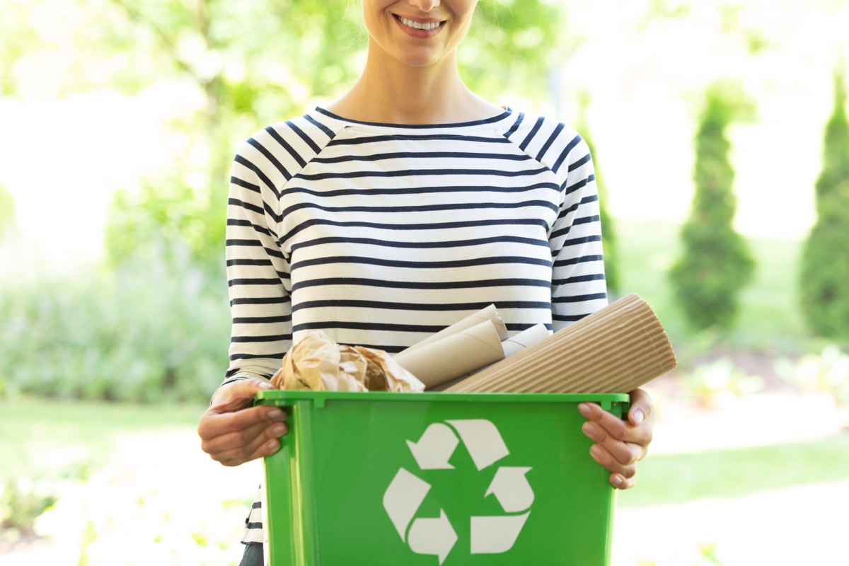 Green box with a recycling sign filled with paper held by a smiling woman