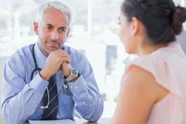 Serious doctor listening to patient explaining her painful in his office